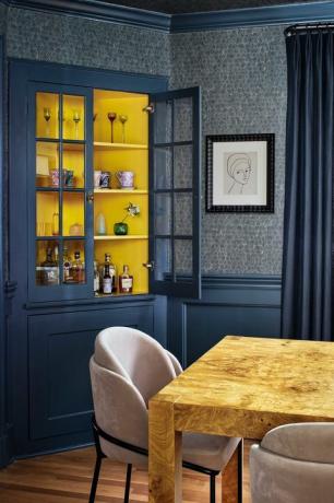 mavi boyalı duvarlar ve lacivert duvar kaplaması ile yemek odası, alkollü bar dolabı, pembe kadife yemek sandalyeleri ile ahşap yemek sandalyesi