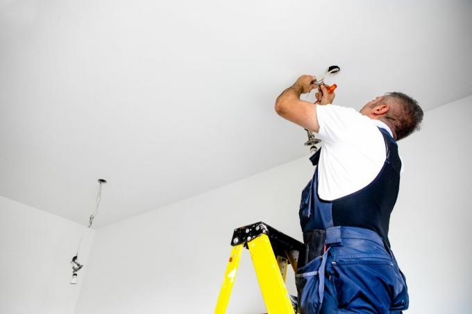bir tamirci bir erkek elektrikçi ışığı tamir ediyor led ışığı tavan armatürüne takıyor